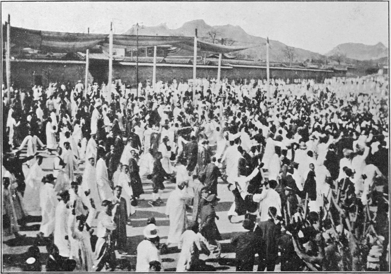 흰 옷을 입은 수천 명의 군중이 기와지붕 담장과 산을 배경으로 넓은 마당을 가득 메운 1919년 흑백 사진.