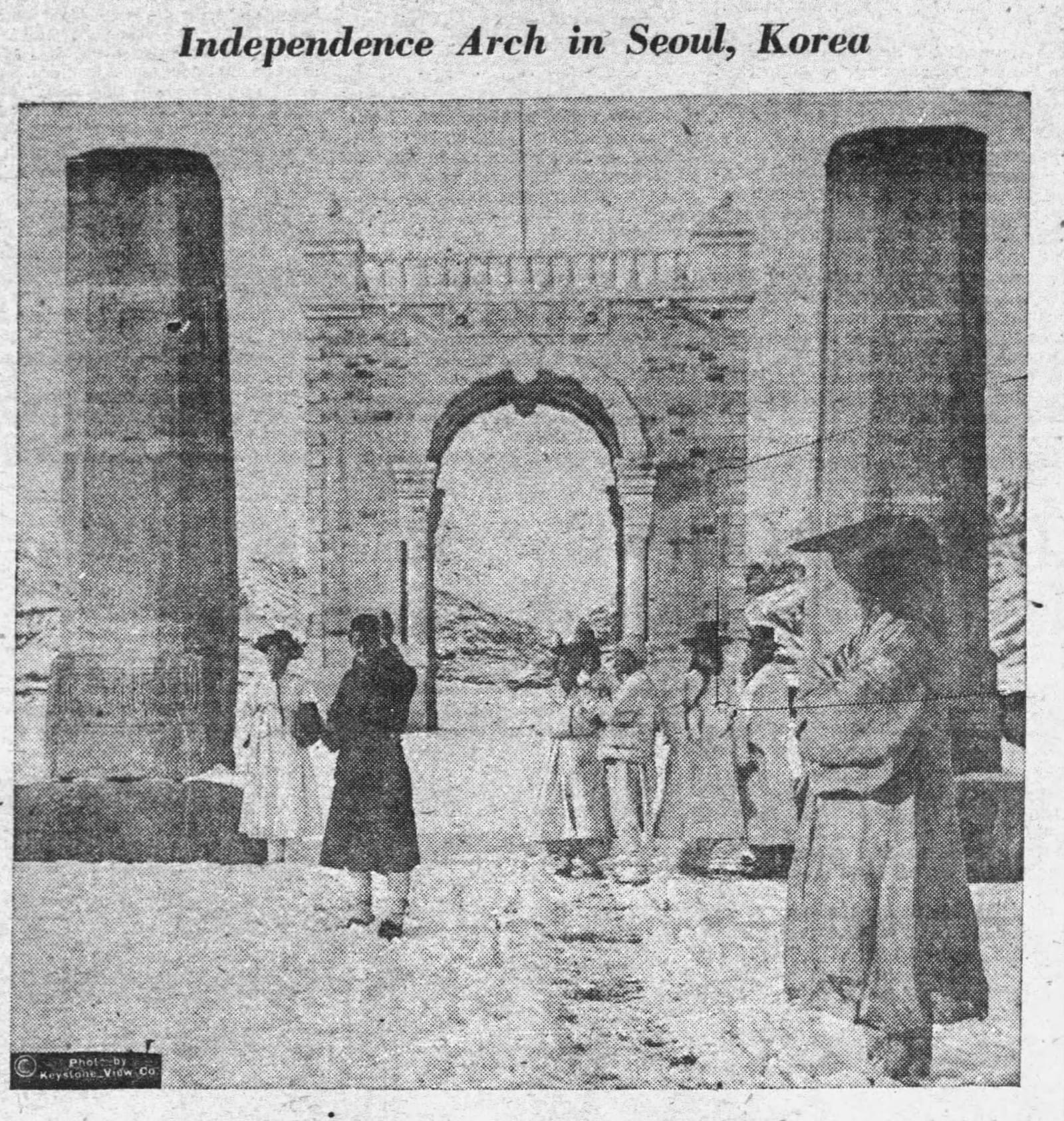 돌기둥 두 개 사이로 아치형 독립문이 서 있고 그 앞을 한복 차림의 사람들이 지나가는 1923년 흑백 사진의 신문 인쇄 도판.
